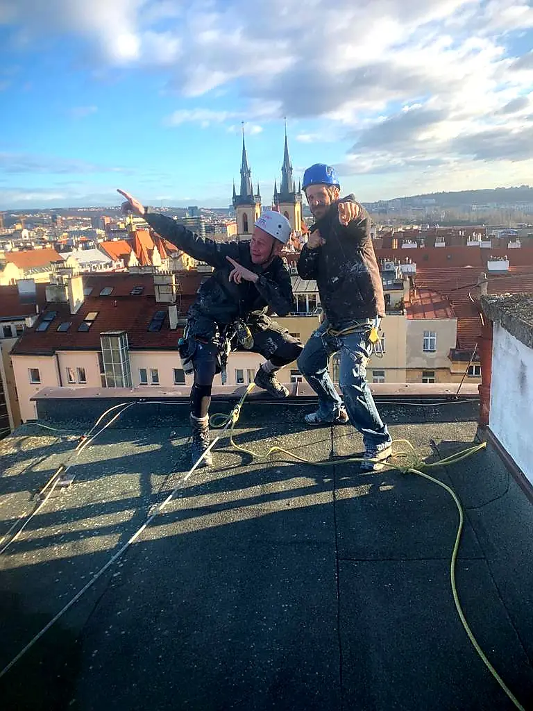 Dva řemeslníci na střeše domu u Staroměstského náměstí, v pozadí Týnský chrám